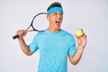 Young hispanic boy playing tennis holding racket and ball angry and mad screaming frustrated and furious, shouting with anger Royalty Free Stock Photo