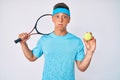 Young hispanic boy playing tennis holding racket and ball puffing cheeks with funny face Royalty Free Stock Photo