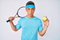 Young hispanic boy playing tennis holding racket and ball relaxed with serious expression on face Royalty Free Stock Photo