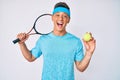 Young hispanic boy playing tennis holding racket and ball smiling and laughing hard out loud because funny crazy joke Royalty Free Stock Photo