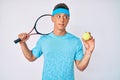 Young hispanic boy playing tennis holding racket and ball smiling looking to the side and staring away thinking Royalty Free Stock Photo