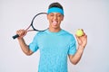 Young hispanic boy playing tennis holding racket and ball sticking tongue out happy with funny expression Royalty Free Stock Photo