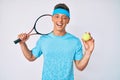 Young hispanic boy playing tennis holding racket and ball winking looking at the camera with sexy expression, cheerful and happy Royalty Free Stock Photo