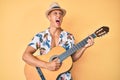 Young hispanic boy wearing summer style playing classical guitar angry and mad screaming frustrated and furious, shouting with Royalty Free Stock Photo