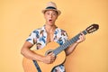 Young hispanic boy wearing summer style playing classical guitar in shock face, looking skeptical and sarcastic, surprised with Royalty Free Stock Photo