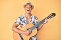 Young hispanic boy wearing summer style playing classical guitar smiling and laughing hard out loud because funny crazy joke