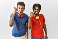Young hispanic brothers standing over isolated background wearing headphones angry and mad raising fist frustrated and furious