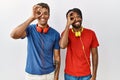 Young hispanic brothers standing over isolated background wearing headphones doing ok gesture with hand smiling, eye looking