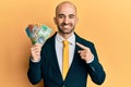 Young hispanic business man holding canadian dollars smiling happy pointing with hand and finger Royalty Free Stock Photo