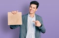 Young hispanic business man holding paper bag with bread smiling happy pointing with hand and finger Royalty Free Stock Photo