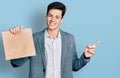 Young hispanic business man holding paper bag with bread smiling happy pointing with hand and finger to the side Royalty Free Stock Photo