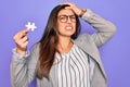 Young hispanic business woman holding puzzle peace as cooperation and union on work stressed with hand on head, shocked with shame