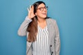 Young hispanic business woman wearing glasses standing over blue isolated background smiling with hand over ear listening an Royalty Free Stock Photo
