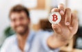 Young hispanic businessman smiling happy holding bitcoin at the office Royalty Free Stock Photo