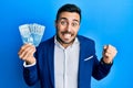 Young hispanic businessman wearing business suit holding chilean pesos banknotes screaming proud, celebrating victory and success Royalty Free Stock Photo