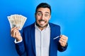 Young hispanic businessman wearing business suit holding denmark krone banknotes screaming proud, celebrating victory and success Royalty Free Stock Photo