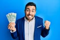 Young hispanic businessman wearing business suit holding polish zloty banknotes screaming proud, celebrating victory and success Royalty Free Stock Photo