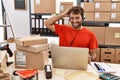 Young hispanic call center agent man working at warehouse smiling confident touching hair with hand up gesture, posing attractive Royalty Free Stock Photo