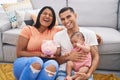 Young hispanic couple with baby holding piggy bank smiling and laughing hard out loud because funny crazy joke Royalty Free Stock Photo