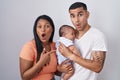 Young hispanic couple with baby standing together over isolated background surprised pointing with finger to the side, open mouth Royalty Free Stock Photo