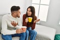 Young hispanic couple drinking coffee sitting on the sofa at home Royalty Free Stock Photo