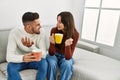 Young hispanic couple drinking coffee sitting on the sofa at home Royalty Free Stock Photo