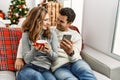 Young hispanic couple drinking coffee using smartphone sitting on the sofa at home Royalty Free Stock Photo