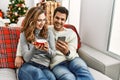 Young hispanic couple drinking coffee using smartphone sitting on the sofa at home Royalty Free Stock Photo