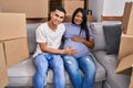 Young hispanic couple expecting a baby sitting on the sofa at new home looking positive and happy standing and smiling with a Royalty Free Stock Photo