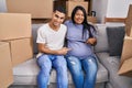 Young hispanic couple expecting a baby sitting on the sofa at new home smiling happy pointing with hand and finger Royalty Free Stock Photo