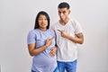 Young hispanic couple expecting a baby standing over background pointing aside worried and nervous with forefinger, concerned and
