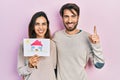 Young hispanic couple holding house draw smiling with an idea or question pointing finger with happy face, number one Royalty Free Stock Photo