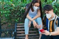 Young Hispanic couple in the park with disposable masks checking their cell phone