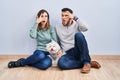 Young hispanic couple sitting on the floor with dog peeking in shock covering face and eyes with hand, looking through fingers Royalty Free Stock Photo