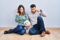 Young hispanic couple sitting on the floor with dog pointing down with fingers showing advertisement, surprised face and open Royalty Free Stock Photo