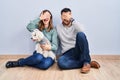Young hispanic couple sitting on the floor with dog smiling and laughing with hand on face covering eyes for surprise Royalty Free Stock Photo