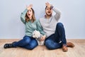 Young hispanic couple sitting on the floor with dog surprised with hand on head for mistake, remember error