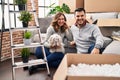Young hispanic couple sitting on the floor at new home with log looking positive and happy standing and smiling with a confident Royalty Free Stock Photo