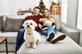 Young hispanic couple smiling happy watching movie sitting on the sofa with dog at home