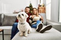 Young hispanic couple smiling happy watching movie sitting on the sofa with dog at home