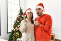 Young hispanic couple standing by christmas tree surprised pointing with finger to the side, open mouth amazed expression Royalty Free Stock Photo