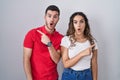 Young hispanic couple standing over isolated background surprised pointing with finger to the side, open mouth amazed expression Royalty Free Stock Photo