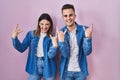 Young hispanic couple standing over pink background shouting with crazy expression doing rock symbol with hands up Royalty Free Stock Photo