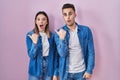 Young hispanic couple standing over pink background surprised pointing with hand finger to the side, open mouth amazed expression Royalty Free Stock Photo