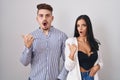 Young hispanic couple standing over white background surprised pointing with hand finger to the side, open mouth amazed expression Royalty Free Stock Photo