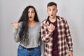 Young hispanic couple standing over white background surprised pointing with hand finger to the side, open mouth amazed expression Royalty Free Stock Photo