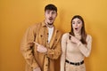 Young hispanic couple standing over yellow background surprised pointing with finger to the side, open mouth amazed expression Royalty Free Stock Photo