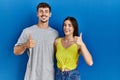 Young hispanic couple standing together over blue background doing happy thumbs up gesture with hand Royalty Free Stock Photo