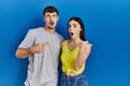 Young hispanic couple standing together over blue background surprised pointing with finger to the side, open mouth amazed Royalty Free Stock Photo