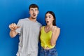 Young hispanic couple standing together over blue background surprised pointing with hand finger to the side, open mouth amazed Royalty Free Stock Photo